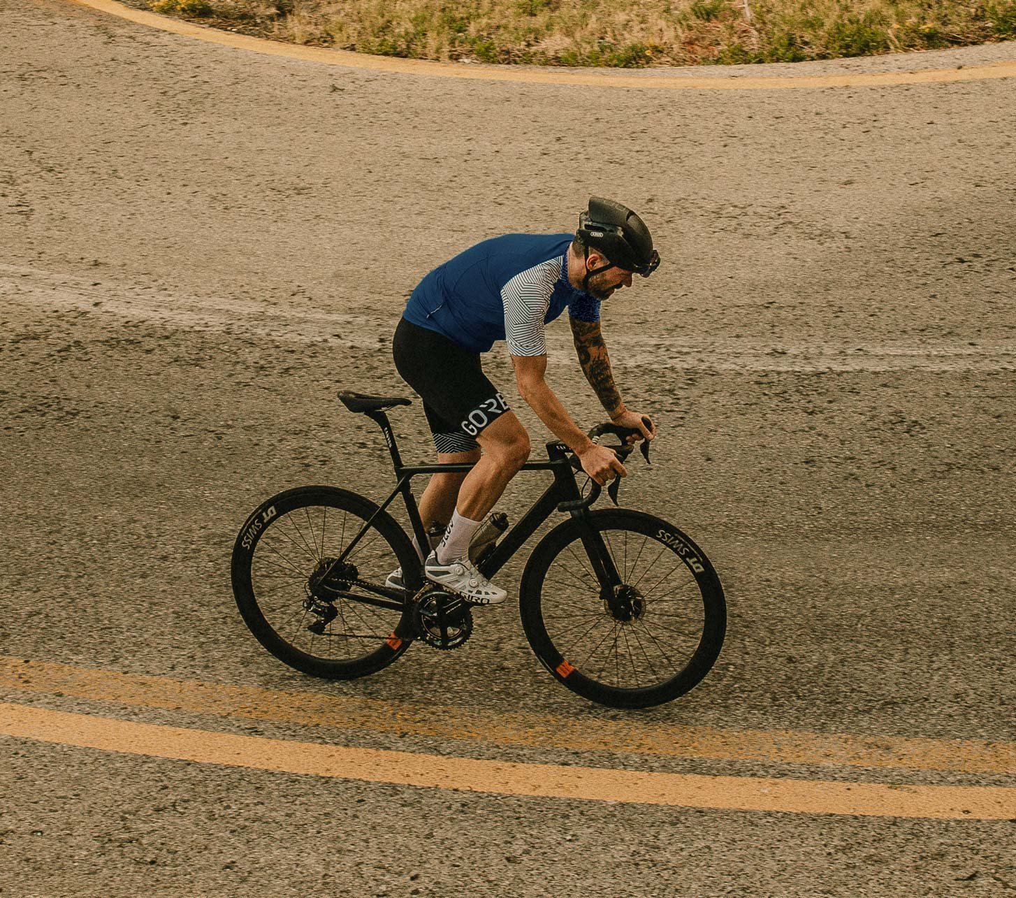 Cycliste sur route portant des vêtements Gore Wear roulant sur une route asphaltée sinueuse vue de dessus