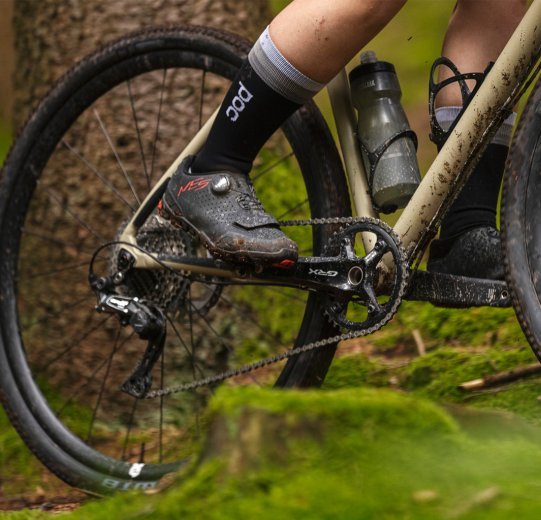 Cyclist riding a gravel bike with GRX shifters across a trail.