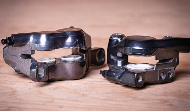 Zwei Bremszangen für Scheibenbremsen am Fahrrad liegen nebeneinander auf einer warmtonigen Holzplatte 