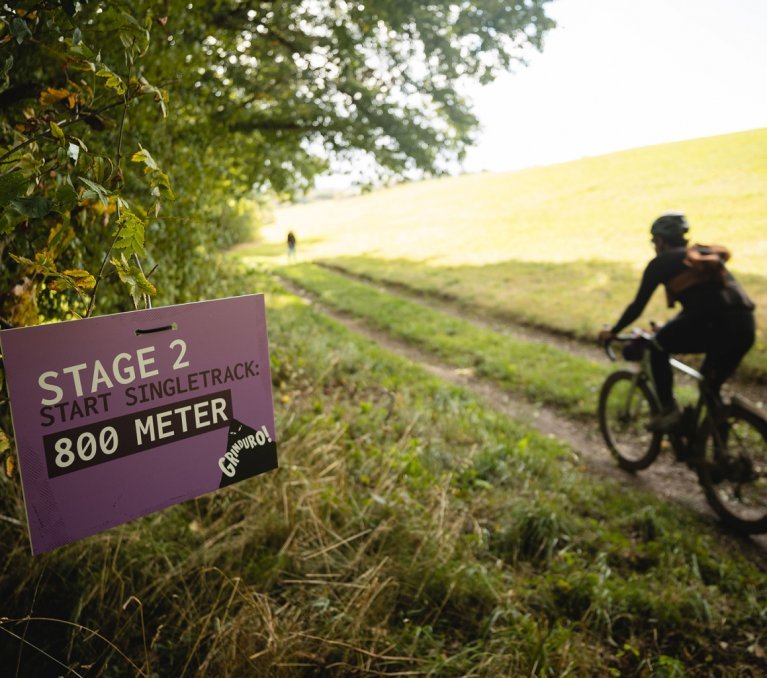 Auf der linken Seite des Waldwegs steht das Hinweis-Schild zur nächsten Stage des Grinduros. Ein Teilnehmer passiert diese Stelle.