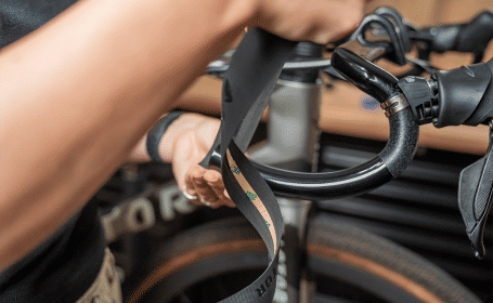 Die Mechanikerin setzt das Lenkerband unterhalb des Lenkers an, die Klebefläche zeigt nach oben zum Lenker. 