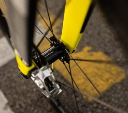 Detailaufnahme einer Vorderradnabe von Black Inc mit Ceramicspeed Logo in einer gelb-schwarzen Carbongabel mit silberfarbener Bremszange.