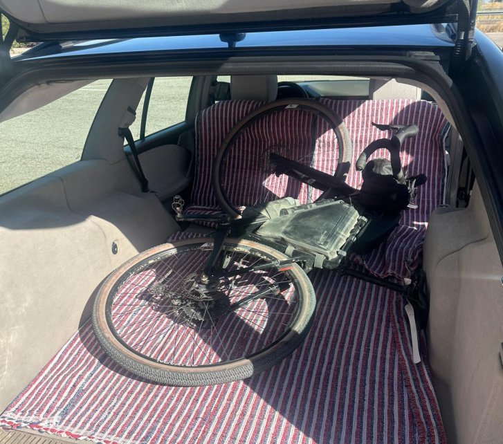 Ein staubiges, graues Gravel-Bike mit Rahmentaschen liegt im Laderaum eines Kombi auf einer rot-weiß-gestreiften Decke