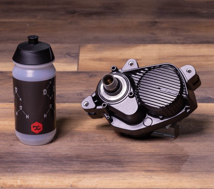 A Shimano EP8 e-bike drive on a dark wooden floor. A bike water bottle stands next to it