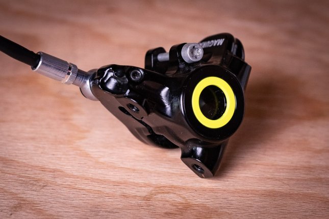 Una pinza de freno Magura negra con un aro amarillo brillante reposa sobre una tabla de madera.