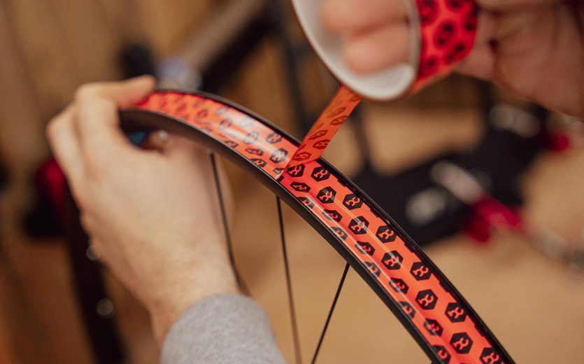 Main posant un fond de jante sous tension dans une jante de vélo, avec plusieurs centimètres de chevauchement.