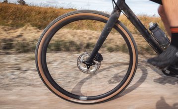 En la imagen, la rueda delantera de una bici Gravel bc original Flint en acción. La bici está siendo conducida por un camino forestal. 