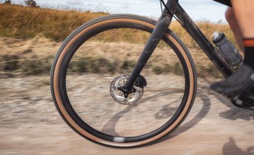 La photo montre la roue avant d'un vélo de gravel bc original Flint en pleine action. Le vélo est en train d'être poussé / roulé sur un chemin de terre. 