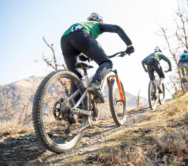 Un grupo de ciclistas de montaña asciende por una cuesta rocosa con tiempo soleado.