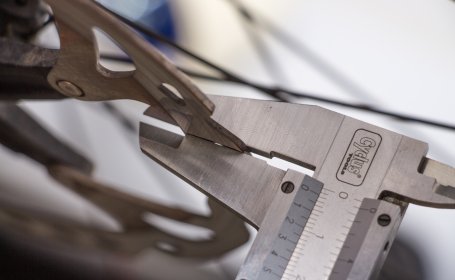 Gros plan sur un disque de frein de vélo dont l’épaisseur est mesurée à l’aide d’un pied à coulisse.