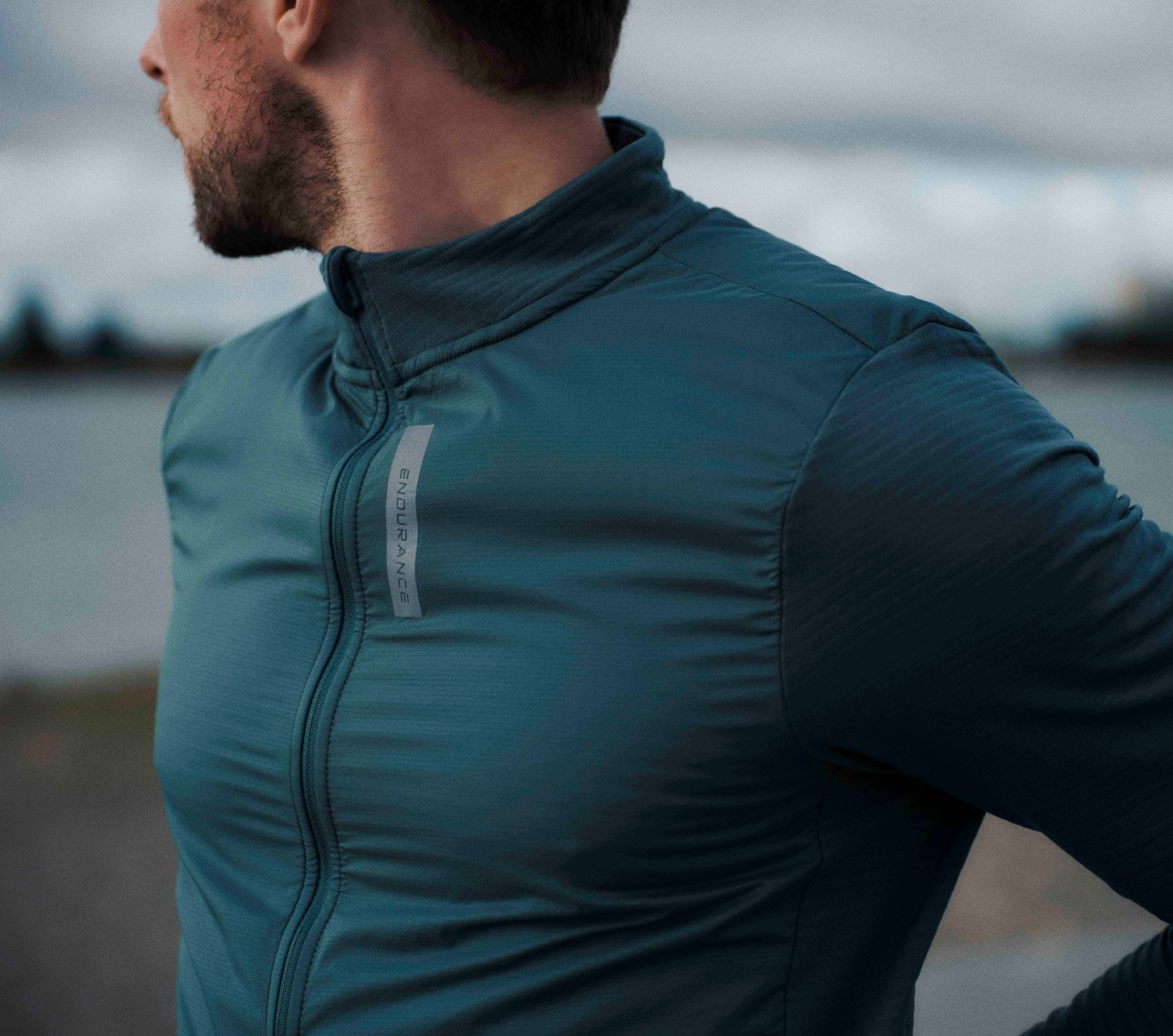 Nahaufnahme eines Mannes in einem blaugrünen Endurance Fahrradtrikot mit langen Ärmeln und Stehkragen.