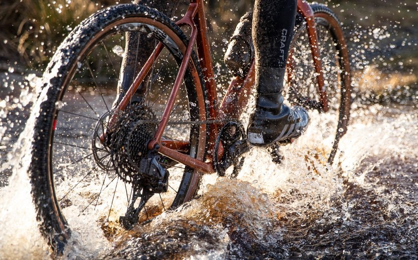 A biker rides through a large puddle.