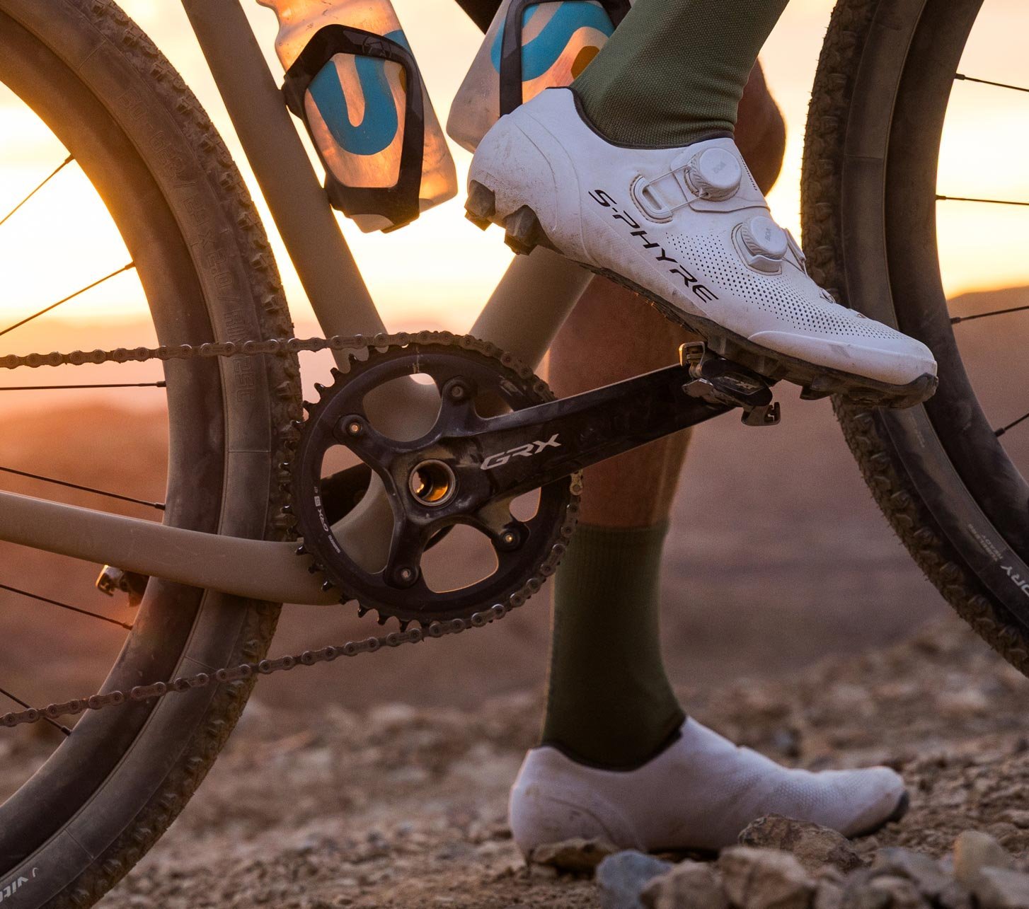 Shimano GRX Di2 en bicicleta gravel sobre un sendero rocoso al atardecer, con enfoque en transmisión y rueda trasera.