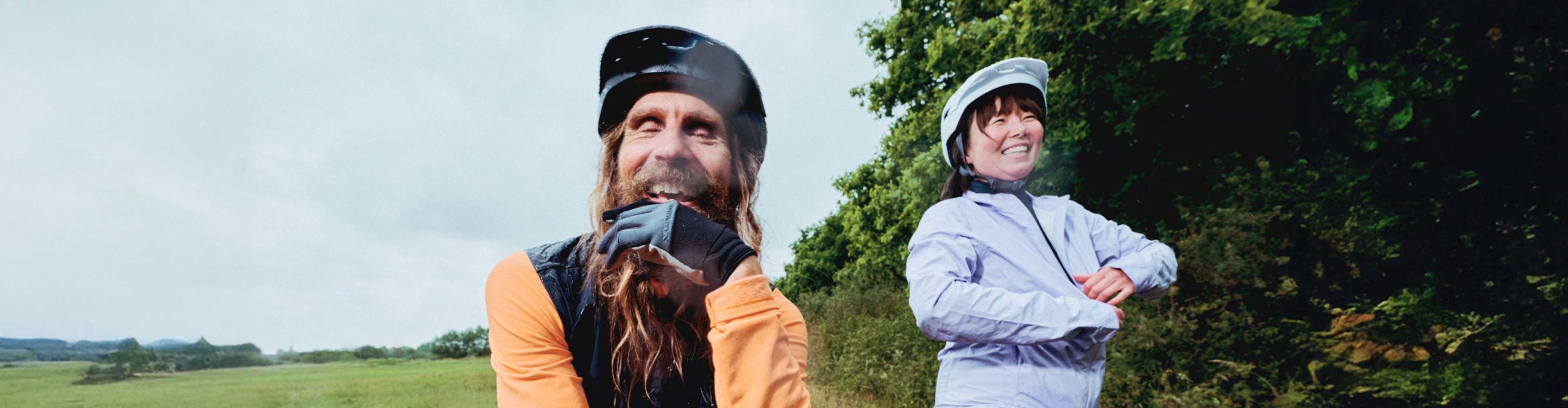 Two smiling cyclists wearing Endura rainwear taking a break on a country lane in wet weather.