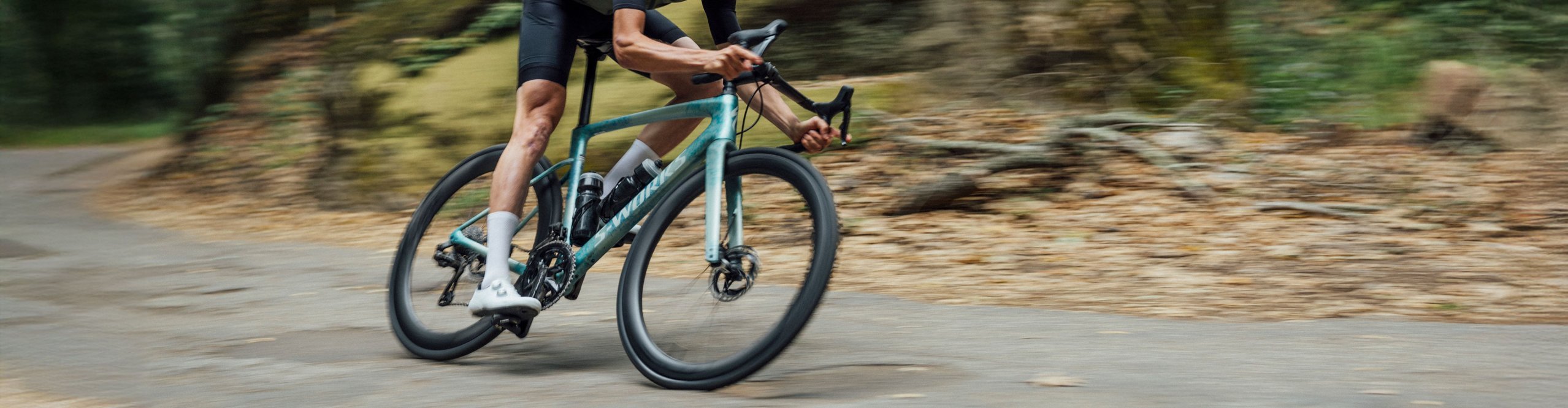 Sportlicher Rennradfahrer in aerodynamischer Position fährt ein Specialized Rennrad auf kurviger Straße im Wald – Performance-Roadbike für ambitioniertes Training und schnelles Straßenfahren.