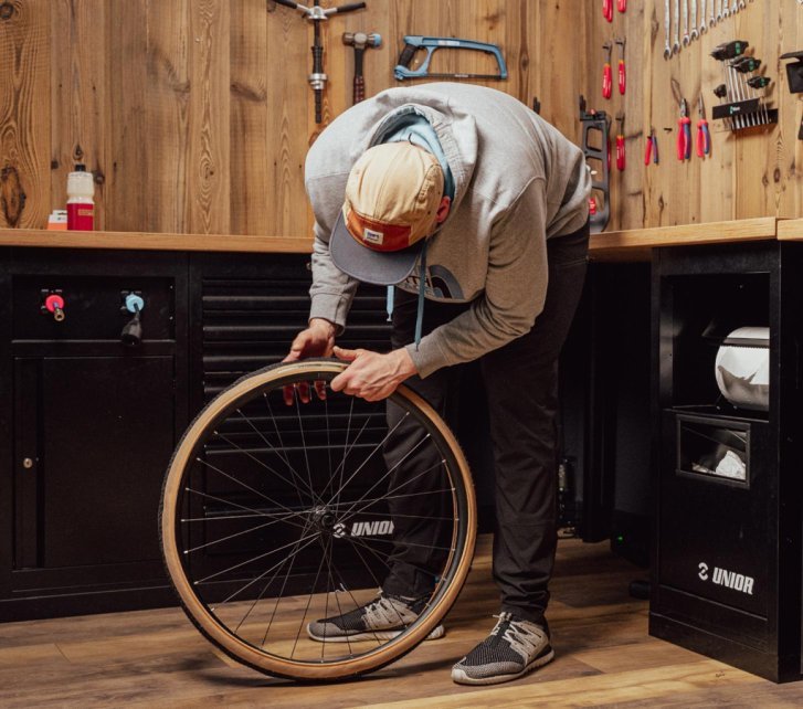 Personne montant un pneu gravel à la main sur une jante de vélo dans un atelier.