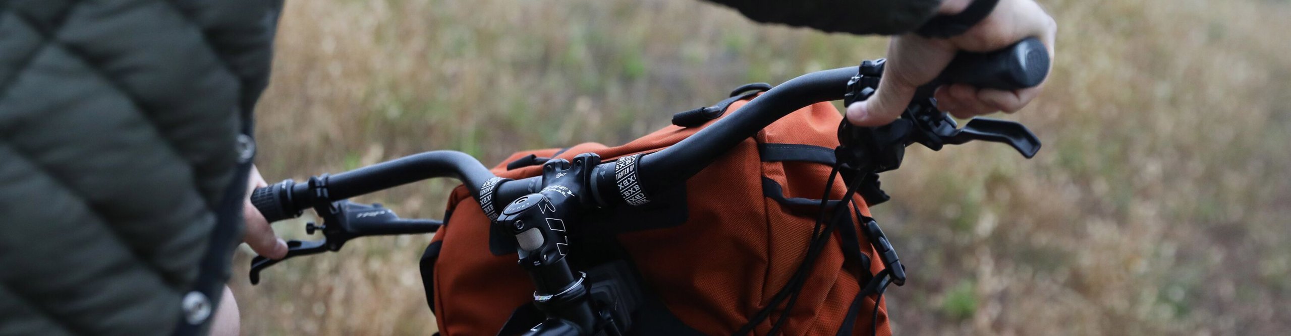 Fahrer greift an den Ritchey Lenker eines Mountainbikes mit Lenkertasche auf einem schmalen Trail.
