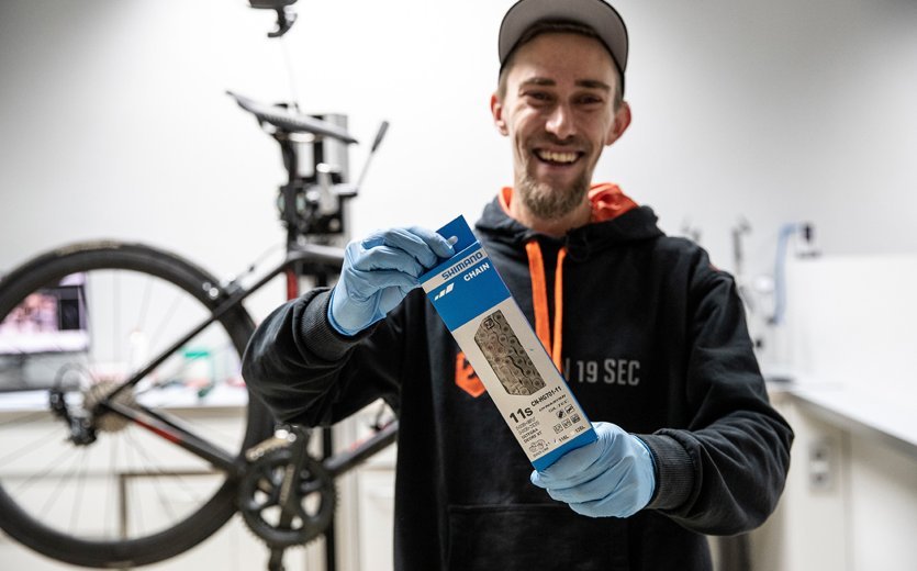 Thomas, mécanicien chez bc, tient une nouvelle chaîne Shimano 11s devant l’appareil photo. 