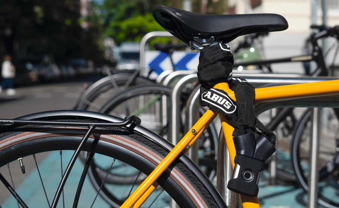 Bicicleta asegurada con un candado ABUS YARDO a un soporte; el candado se abre mediante sensor de huella dactilar.