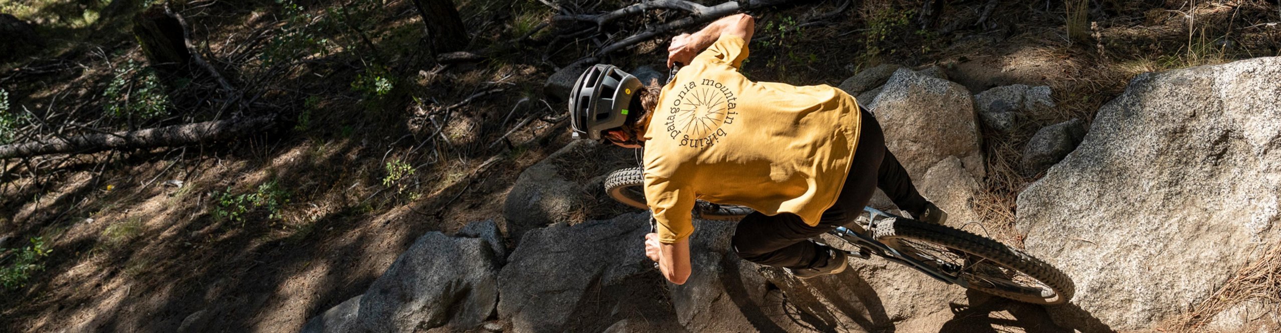 Vététiste portant un t-shirt Patagonia jaune roulant sur un sentier rocheux technique en forêt