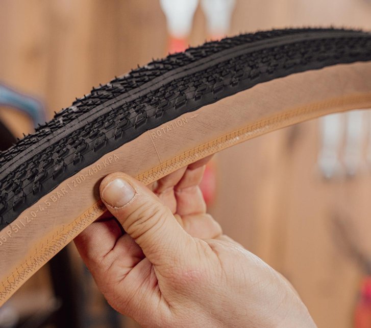 Main tenant un pneu gravel Specialized Pathfinder, avec la flèche indiquant le sens de rotation visible sur le flanc.