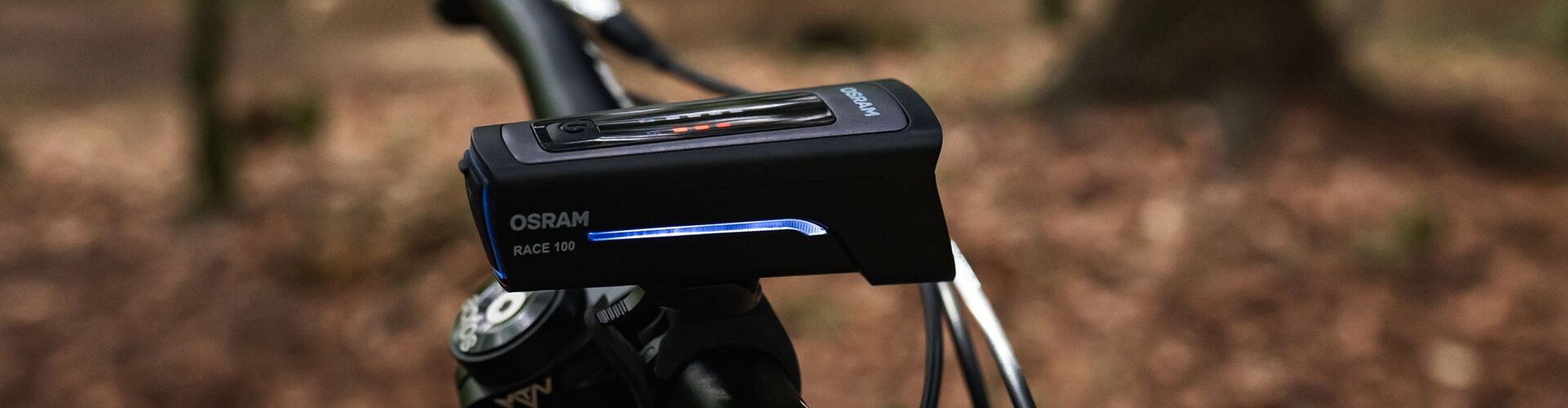 OSRAM Race 100 bike light on the handlebar – detail shot with forest background