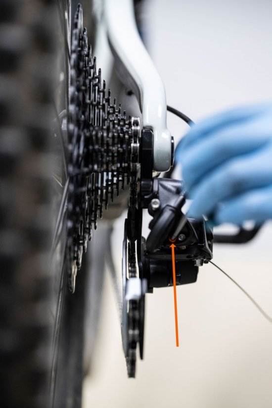 Using an Allen key, bc mechanic Thomas adjusts the inner derailleur limit screw. An orange arrow marks the exact position.