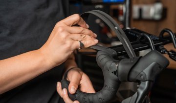 Die Mechanikerin wickelt das Lenkerband um den Oberlenker.