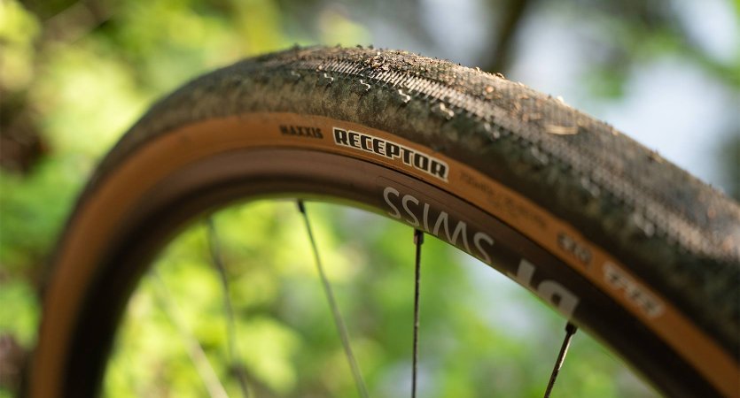 Gros plan d’un pneu gravel à flanc beige avec bande centrale à profil bas, marquage « Receptor » visible sur le flanc.