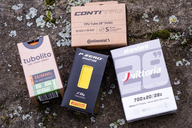 Vier Fahrradschläuche in ihren Kartons liegen auf einem Stein: Conti TPU, Tubolito Gravelm Pirelli P-Zero Smartube, Vittoria Standard