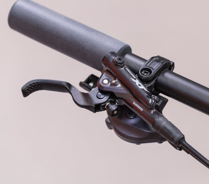 Vista superior del extremo derecho de un manillar de bicicleta con puño de goma y una bomba de freno Shimano XT con cilindro maestro.