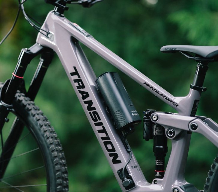 Close-up of a grey Transition Regulator SX E-MTB in the forest: focus on the Bosch range extender mounted on the bottle cage in the frame triangle
