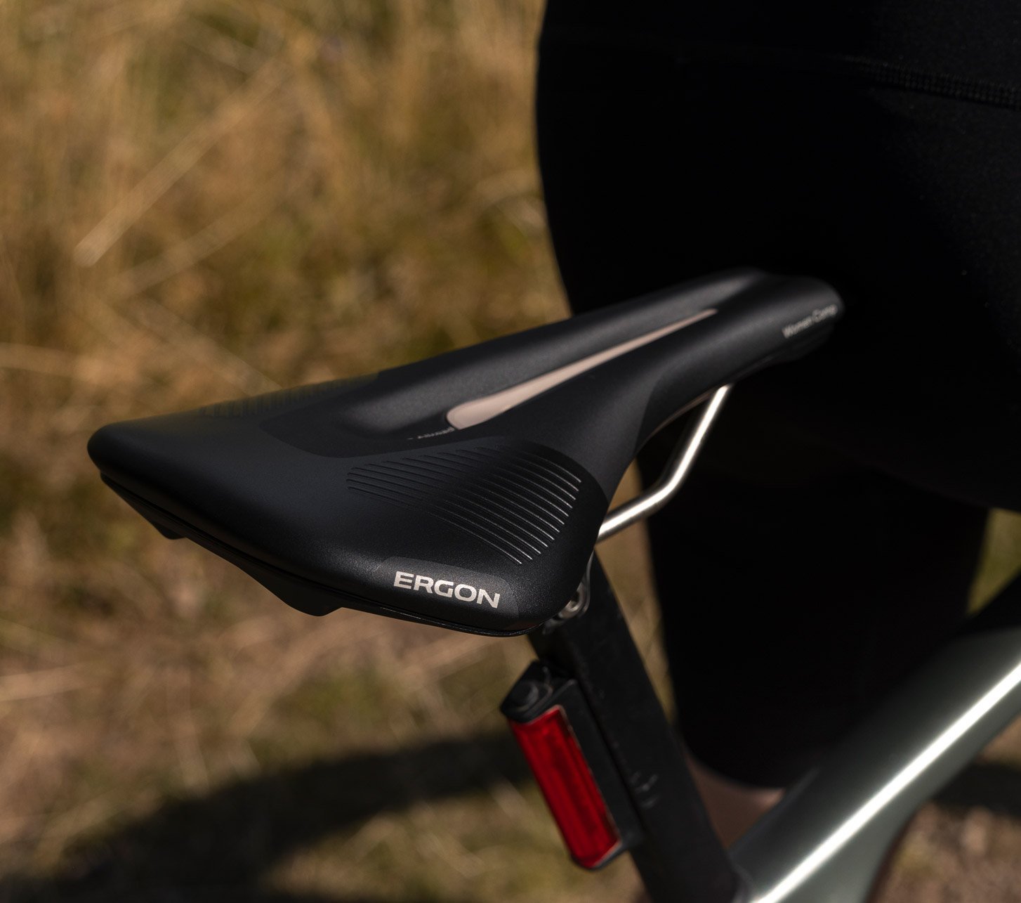 Nahaufnahme eines schwarzen Ergon SR Allroad Woman Fahrradsattels am Rennrad oder Gravelbike, daneben eine Fahrerin in Radhose.
