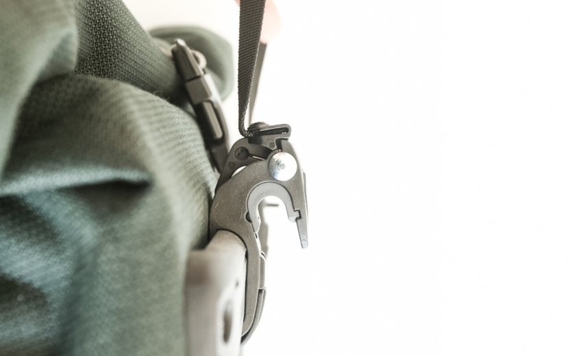 Nahaufnahme des Befestigungssystems einer grünen Ortlieb Back-Roller Urban Fahrradtasche. Eine Hand zieht den schwarzen Verschlussgurt, während das Haken-System für die Montage am Gepäckträger sichtbar ist.