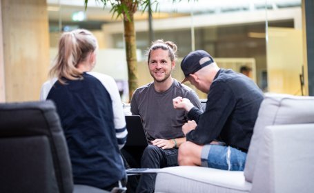 Drei Personen sitzen in einem modernen Bürobereich zusammen und Brainstormen in entspannter Atmosphäre