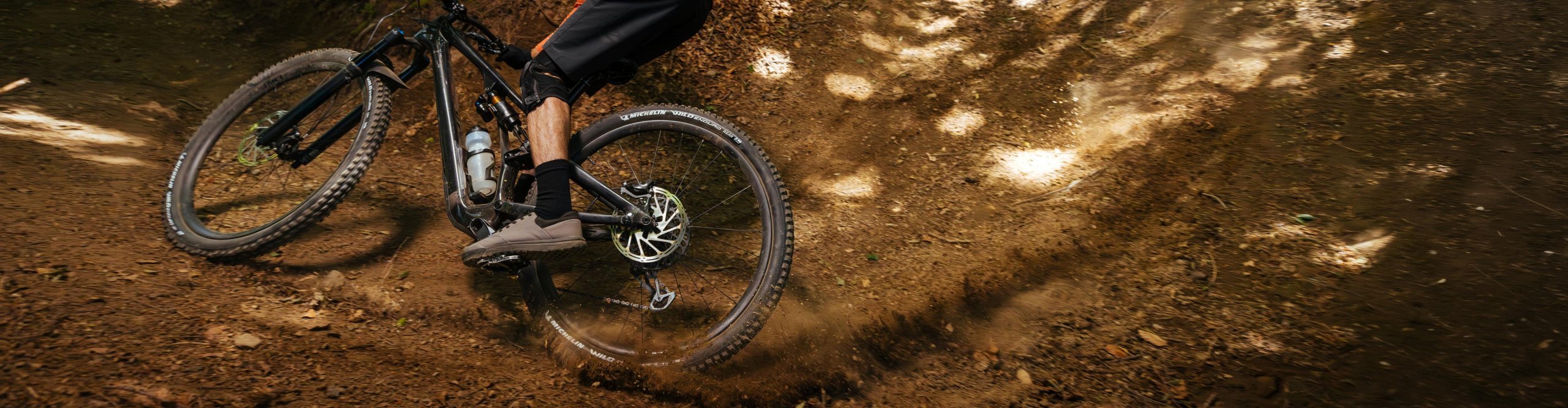 Michelin Wild Enduro Performance tires on a mountain bike riding a dusty forest enduro trail with strong grip, control and off-road traction
