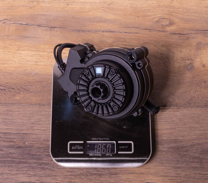 A TQ HPR50 e-bike drive on a kitchen scale on a dark wooden floor. Display shows 1,860 grams