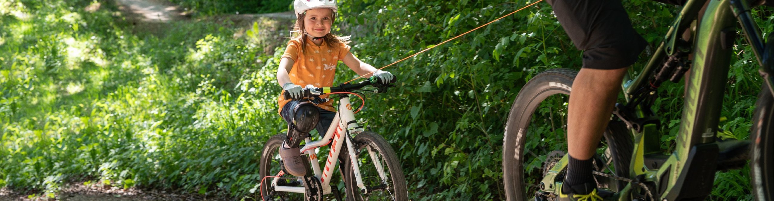 Kind wird mit dem kommit Bike-Zugsystem vom Papa hinter dem Fahrrad gezogen.