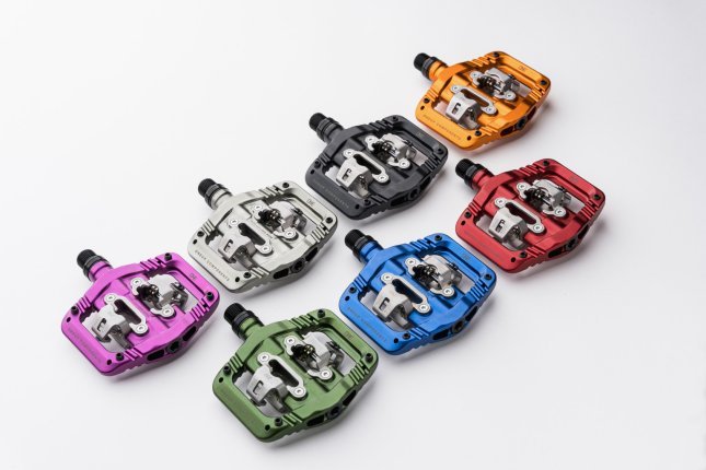 Seven colorful OneUp Clip Pedals for MTB lie side by side on a white surface.