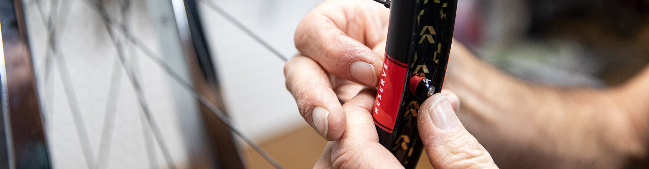 Close-up: hands applying tubeless rim tape to a Reserve bicycle wheel rim.