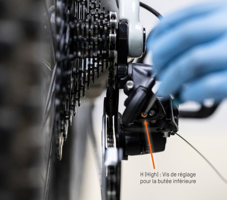 Thomas, le mécanicien de bc, utilise une clef hexagonale pour déplacer la butée intérieure du dérailleur. Une flèche orange marque l'endroit exact.