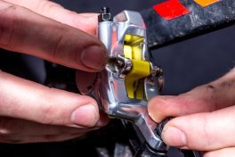 The yellow bleed block is positioned between the brake pads, while the hands hold the silver brake caliper.
