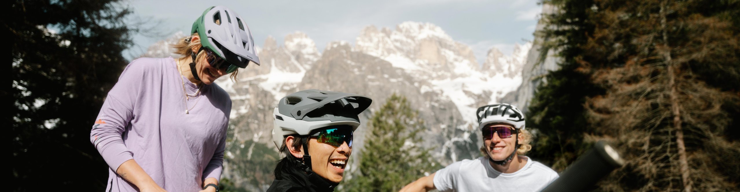Three mountain bikers take a break wearing the Alpina Rootage 2 Mips helmet with snowy Alps in the background.