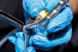 A hand wearing blue gloves opens the fill port of a hydraulic disc brake on a bicycle with a 1/4 turn.