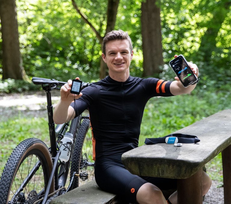 Christof, de gestión de productos de bc, sosteniendo frente a la cámara un ciclocomputador Garmin Edge y su smartphone, que muestra sus datos de rendimiento.