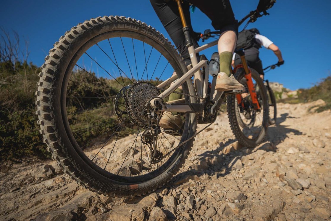 Dos ciclistas de montaña rodando por un sendero rocoso con piedras sueltas.