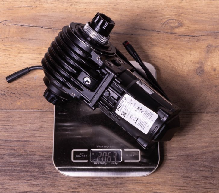 A Fazua Ride 60 e-bike drive on a kitchen scale on a dark wooden floor. Display shows 2,063 grams