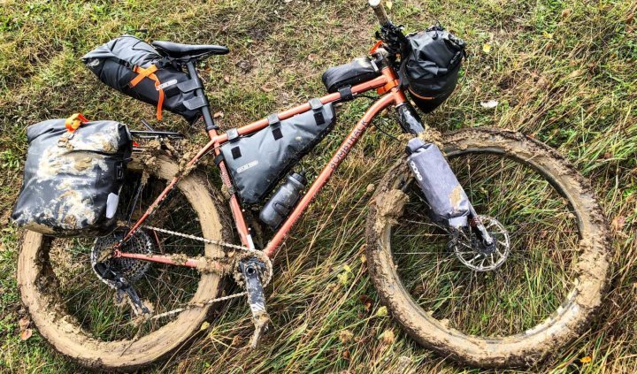 Un vélo gravel boueux avec des sacoches repose sur une prairie après une sortie.
