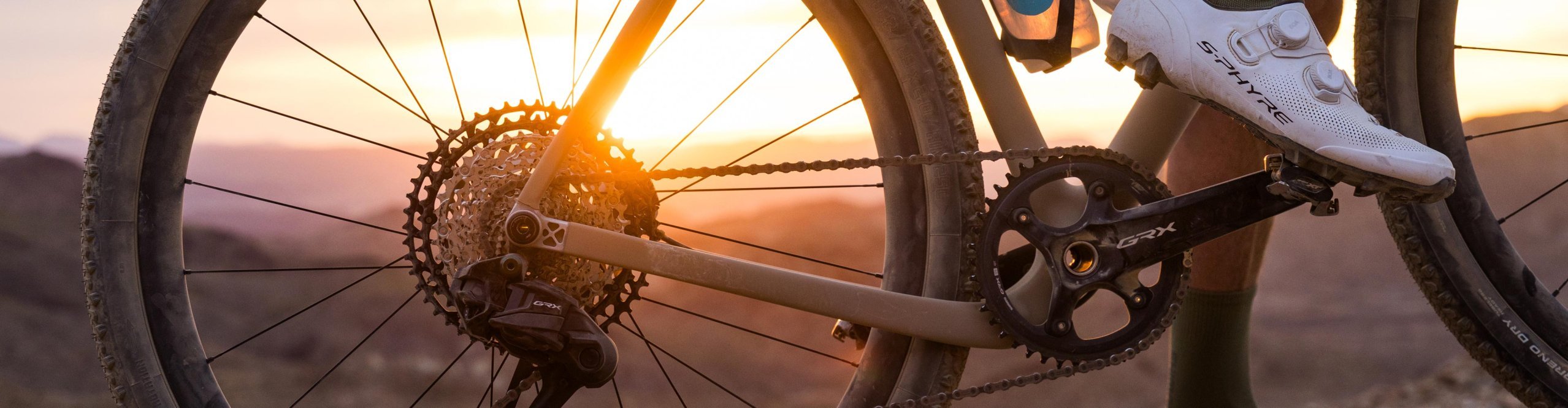 Shimano GRX Di2 en bicicleta gravel sobre un sendero rocoso al atardecer, con enfoque en transmisión y rueda trasera.