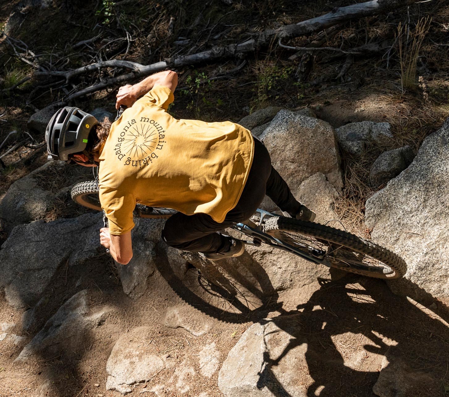 Vététiste portant un t-shirt Patagonia jaune roulant sur un sentier rocheux technique en forêt